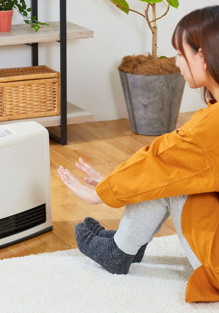 Woman Warming Her Hands By Heater In Orange Shirt